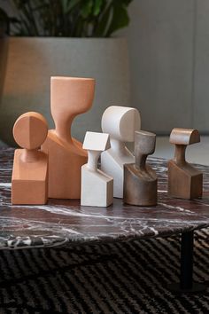 three wooden figures sitting on top of a marble table next to a chair and potted plant