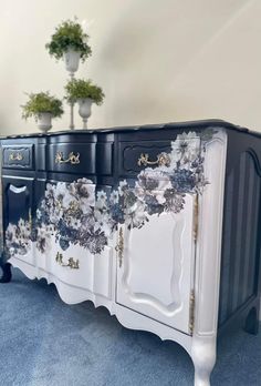 a black and white sideboard with flowers painted on the front, sitting in a blue carpeted room