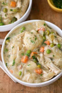 two white bowls filled with chicken and dumplings on top of a wooden table next to a bowl of soup