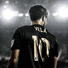 a man standing in front of a stadium filled with people wearing black and gold shirts