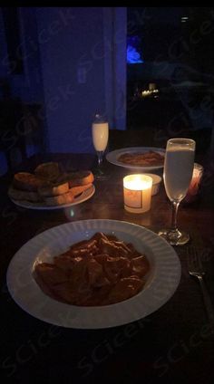 a table topped with plates of food next to glasses of wine and candlelight candles