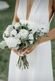 a woman in a white dress holding a bouquet of flowers and greenery on her wedding day