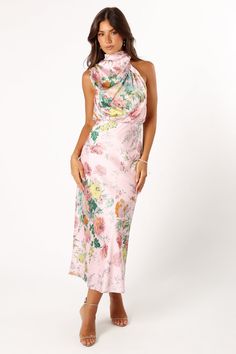 a woman wearing a pink floral print dress with high neck and low cut back, standing in front of a white background