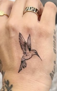 a small bird tattoo on the left wrist and right hand is shown in black ink