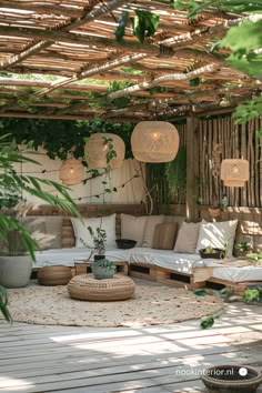 an outdoor living area with lots of plants and pillows on the floor, in front of a pergolated roof