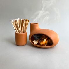 a clay pot with matches in it next to a small cup filled with matchsticks