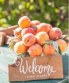 a wooden sign that says welcome with some peaches in the basket behind it on a table