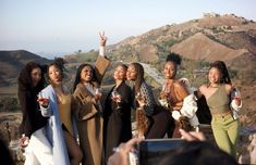 a group of women standing next to each other on top of a hill with drinks in their hands