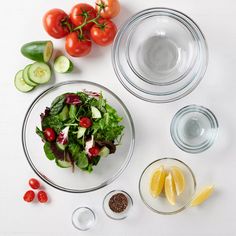 a white table topped with plates and bowls filled with salad ingredients next to sliced cucumbers