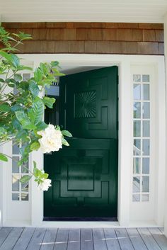 a green door with white flowers in front of it on the side of a house