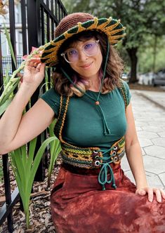 a woman wearing a hat and glasses sitting on the ground next to a black fence