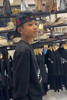 a young boy standing in front of a rack full of shoes and other clothing items