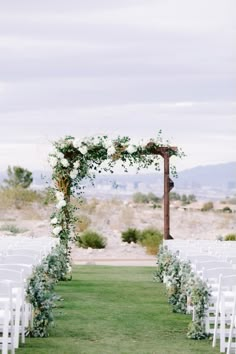 an outdoor ceremony setup with white chairs and greenery