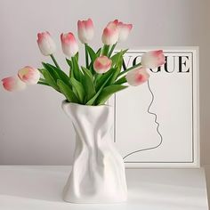 a white vase with pink tulips in it on a table next to a magazine