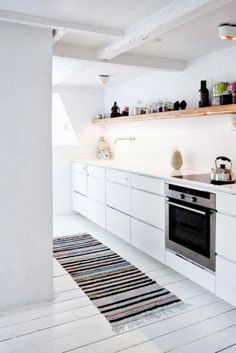 a kitchen with white cabinets and an oven in the center, along with a striped rug on the floor