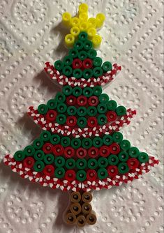 a christmas tree made out of buttons on top of a white tablecloth with a red, green and yellow ribbon