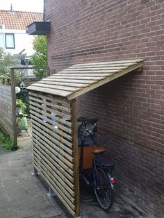 a bike parked under a wooden shelter on the side of a brick building next to a sidewalk