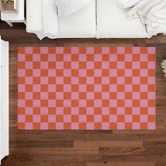 an orange and pink checkered rug is on the floor next to a white bed