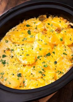 a crock pot filled with cheesy potatoes on top of a wooden table