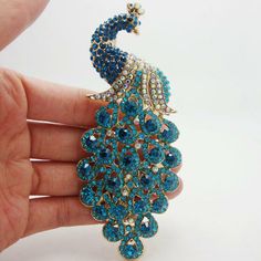 a peacock brooch sitting on top of a person's hand in front of a white background