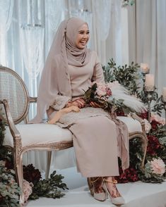 a woman wearing a hijab sitting on a chair with flowers and candles in the background