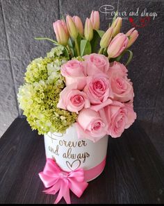 pink roses and green hydrangeas in a white vase with a bow on the side