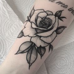 a black and white rose tattoo on the right arm, with words written below it