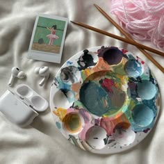 an artist's palette and earphones on top of a bed with pink yarn