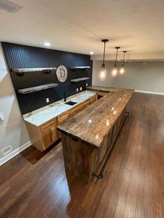 an empty kitchen with wooden floors and counter tops in the middle of the room is lit by pendant lights