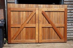 two wooden doors are open in front of a brick building and trash can is next to it