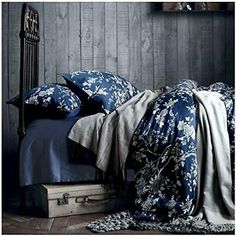 a bed with blue sheets and pillows on top of it next to a wooden wall