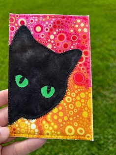 a hand holding up a small patch with a black cat's face on it