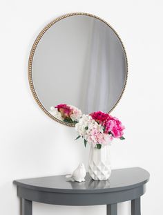 a round mirror sitting on top of a table next to a vase filled with flowers