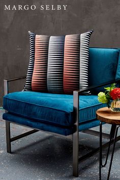 a blue chair with three pillows on it and a table with flowers in front of it