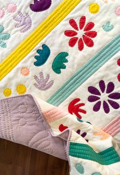 a close up of a quilt on a bed with wood flooring in the background