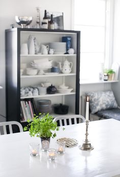 a dining room table with two candles and some dishes on the shelves in front of it