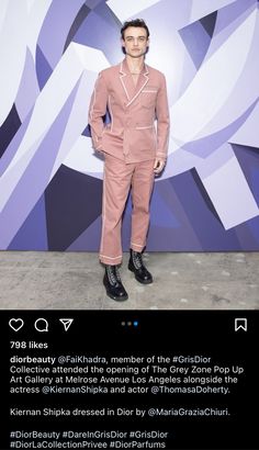 a man standing in front of a purple wall wearing a pink suit and black boots