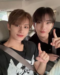 two young men sitting in the back seat of a car, one giving the peace sign