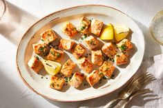 a white plate topped with cut up fish and lemon wedges next to a glass of water