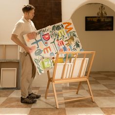 a man standing next to an easel holding up a painting on it's side