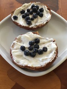 two pieces of bread with cream and blueberries on them sitting on a white plate