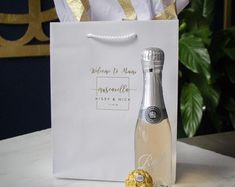 a bottle of champagne sitting on top of a table next to a white bag with gold ribbon