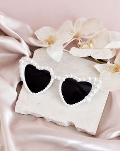 a pair of heart shaped sunglasses sitting on top of a white cloth next to flowers