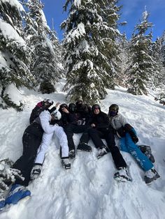 four snowboarders are laying in the snow near some trees and one is taking a selfie