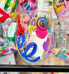 several colorful wine glasses are on display in a store window, one is painted and the other has been decorated