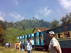 several people are standing in front of a train that is on the tracks near some hills