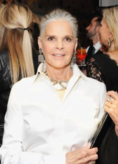 an older woman with grey hair and white shirt standing in front of other women at a party