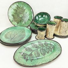 a group of green plates and cups on top of a white tablecloth with leaves painted on them