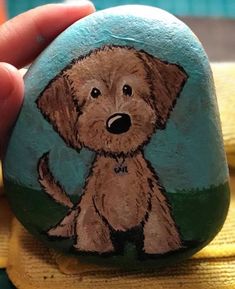 a hand holding a painted rock with a dog on it