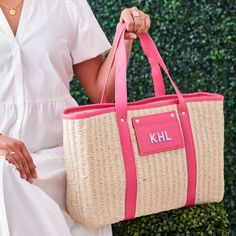 a woman holding a pink and white tote bag in front of a green bush